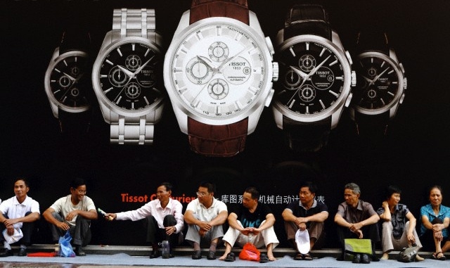 A group of Chinese men sitting in front of a fancy watch billboard